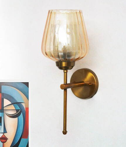 Wall-mounted brass sconce with ribbed glass shade casting warm ambient light beside a colorful abstract portrait on a white wall