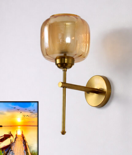 Modern light fixture wall sconce with amber glass shade and brass finish, casting warm light beside a sunset landscape wall art on a white wall