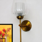 Ribbed Glass Lamp wall light with clear textured glass shade and brushed gold metal base mounted on a white wall, providing elegant ambient lighting for modern interiors.