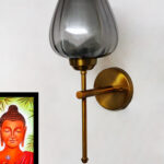 Wall-mounted lamp with a smoked glass shade and brushed gold metal base, providing soft ambient lighting on a white wall.