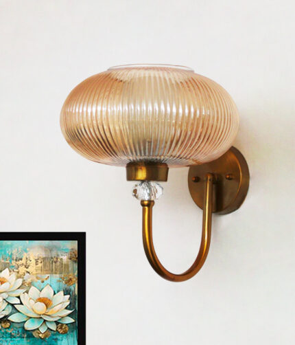 Brass wall sconce with curved metal arm and amber ribbed glass shade mounted on a white wall, casting warm ambient light in a modern interior.