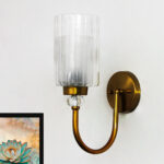 Wall Sconce with clear ribbed glass cylinder shade and gold curved arm mounted on a white wall