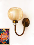 Amber Glass Globe wall sconce with ribbed glass shade and gold curved arm glowing warmly on a white wall