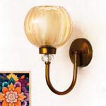 Amber Glass Globe wall sconce with ribbed glass shade and gold curved arm glowing warmly on a white wall