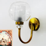Gold wall sconce with curved arm and textured glass shade mounted on a white wall, providing warm ambient lighting.