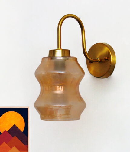 Vintage brass wall sconce with curved arm and amber glass shade mounted on a white wall, casting warm ambient light.