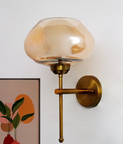 Big Kachori Glass wall light with amber dome-shaped glass shade and brass metal mount installed on a white wall, creating a warm ambient glow beside a framed artwork