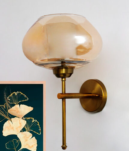 Small Kachori Glass wall light featuring a rounded amber glass shade with a brass metal mount, installed on a white wall beside a decorative floral artwork, emitting warm ambient lighting.