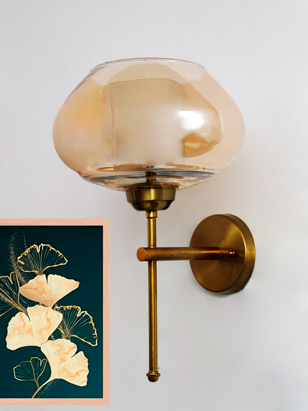 Small Kachori Glass Vintage Globe Wall Sconce Brass Light Small Kachori Glass wall light featuring a rounded amber glass shade with a brass metal mount, installed on a white wall beside a decorative floral artwork, emitting warm ambient lighting.