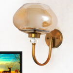 Designer Globe wall light with amber glass shade and brass finish mounted on a wall, featuring a curved arm and warm ambient lighting