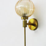 Brass wall light with amber ribbed glass globe shade mounted on a wall, featuring a sleek gold finish and modern decorative design