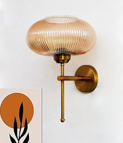 Modern brushed brass wall sconce with ribbed amber glass shade, mounted on a white wall, providing warm ambient lighting for contemporary interiors