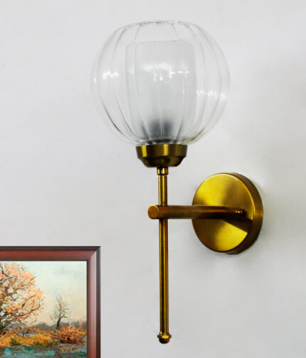 Clear Glass Wall Light with a rounded transparent glass shade and brushed brass arm, mounted on a white wall, providing soft ambient lighting in a modern interior setting