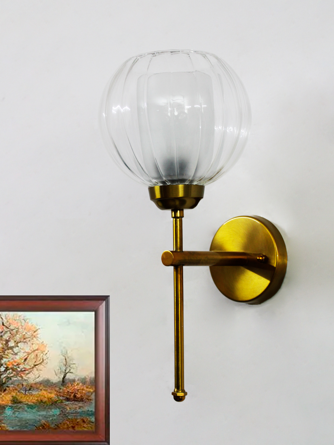 Decorative Brass Wall Sconce Clear Glass Wall Light Clear Glass Wall Light with a rounded transparent glass shade and brushed brass arm, mounted on a white wall, providing soft ambient lighting in a modern interior setting