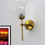 Contemporary Brass Wall Light with clear glass shade mounted on a white wall, featuring a sleek gold finish and modern minimalist design.