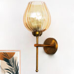 Amber Glass Lamp wall light with textured amber glass shade and brass finish, mounted on a white wall, giving a warm and cozy glow.