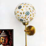Elegant gold wall-mounted mosaic lamp with spherical glass shade featuring intricate geometric and floral patterns, casting warm ambient light on a modern interior wall.