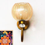 Amber Glass Globe wall sconce with ribbed glass shade and gold curved arm glowing warmly on a white wall