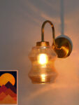 Vintage brass wall sconce with curved arm and amber glass shade mounted on a white wall, casting warm ambient light.