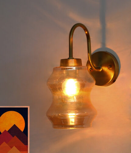 Vintage brass wall sconce with curved arm and amber glass shade mounted on a white wall, casting warm ambient light.