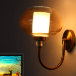 Designer Globe wall light with amber glass shade and brass finish mounted on a wall, featuring a curved arm and warm ambient lighting