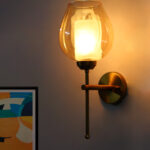 Modern wall sconce with amber glass shade and gold metal base, providing warm ambient lighting on a clean minimalist interior wall.