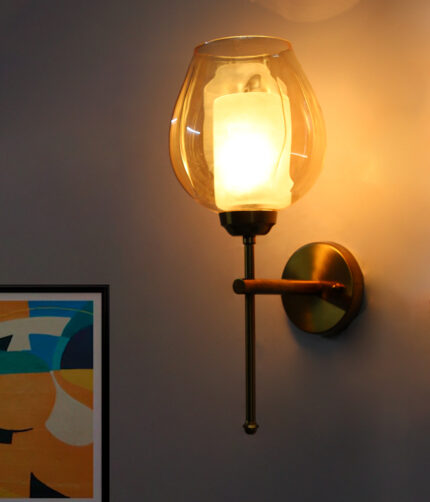 Modern wall sconce with amber glass shade and gold metal base, providing warm ambient lighting on a clean minimalist interior wall.