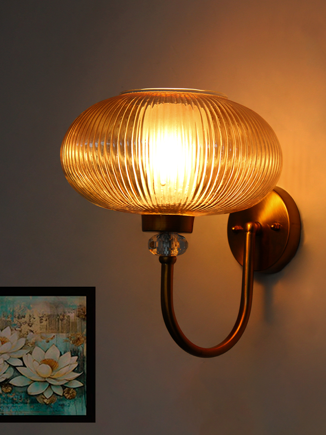 Brass Wall Sconce with Ribbed Amber Glass Shade Brass wall sconce with curved metal arm and amber ribbed glass shade mounted on a white wall, casting warm ambient light in a modern interior.