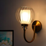 Clear Glass Globe wall sconce with ribbed glass shade and gold curved arm mounted on a white wall