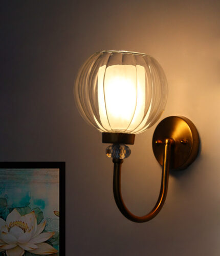 Clear Glass Globe wall sconce with ribbed glass shade and gold curved arm mounted on a white wall