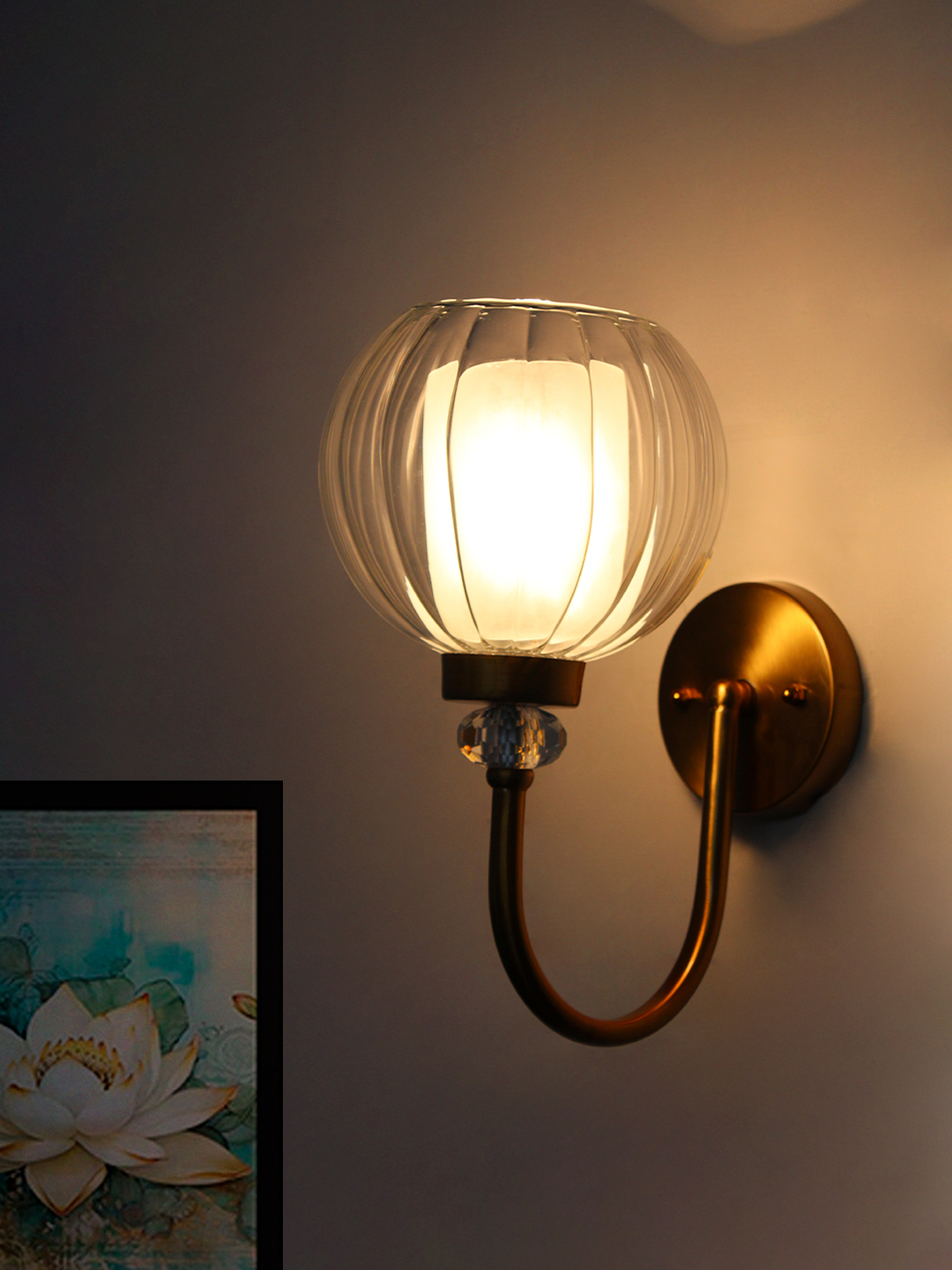 Decorative Brass Wall Light with Clear Glass Globe Clear Glass Globe wall sconce with ribbed glass shade and gold curved arm mounted on a white wall