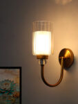 Wall Sconce with clear ribbed glass cylinder shade and gold curved arm mounted on a white wall