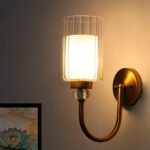Wall Sconce with clear ribbed glass cylinder shade and gold curved arm mounted on a white wall