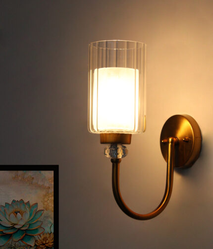 Wall Sconce with clear ribbed glass cylinder shade and gold curved arm mounted on a white wall