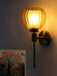 Brass wall light with amber ribbed glass globe shade mounted on a wall, featuring a sleek gold finish and modern decorative design
