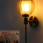 Brass wall light with amber ribbed glass globe shade mounted on a wall, featuring a sleek gold finish and modern decorative design