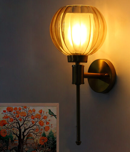 Brass wall light with amber ribbed glass globe shade mounted on a wall, featuring a sleek gold finish and modern decorative design