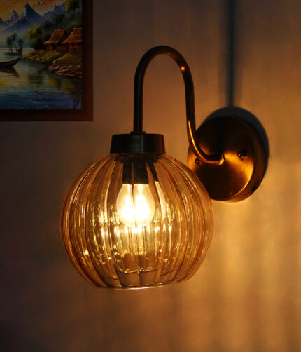 Brass wall sconce with curved arm and ribbed amber glass globe shade mounted on a white wall, providing warm ambient lighting.