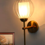 Clear Glass Wall Light with a rounded transparent glass shade and brushed brass arm, mounted on a white wall, providing soft ambient lighting in a modern interior setting