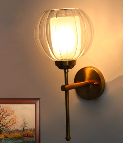 Clear Glass Wall Light with a rounded transparent glass shade and brushed brass arm, mounted on a white wall, providing soft ambient lighting in a modern interior setting