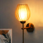 Amber Glass Lamp wall light with textured amber glass shade and brass finish, mounted on a white wall, giving a warm and cozy glow.