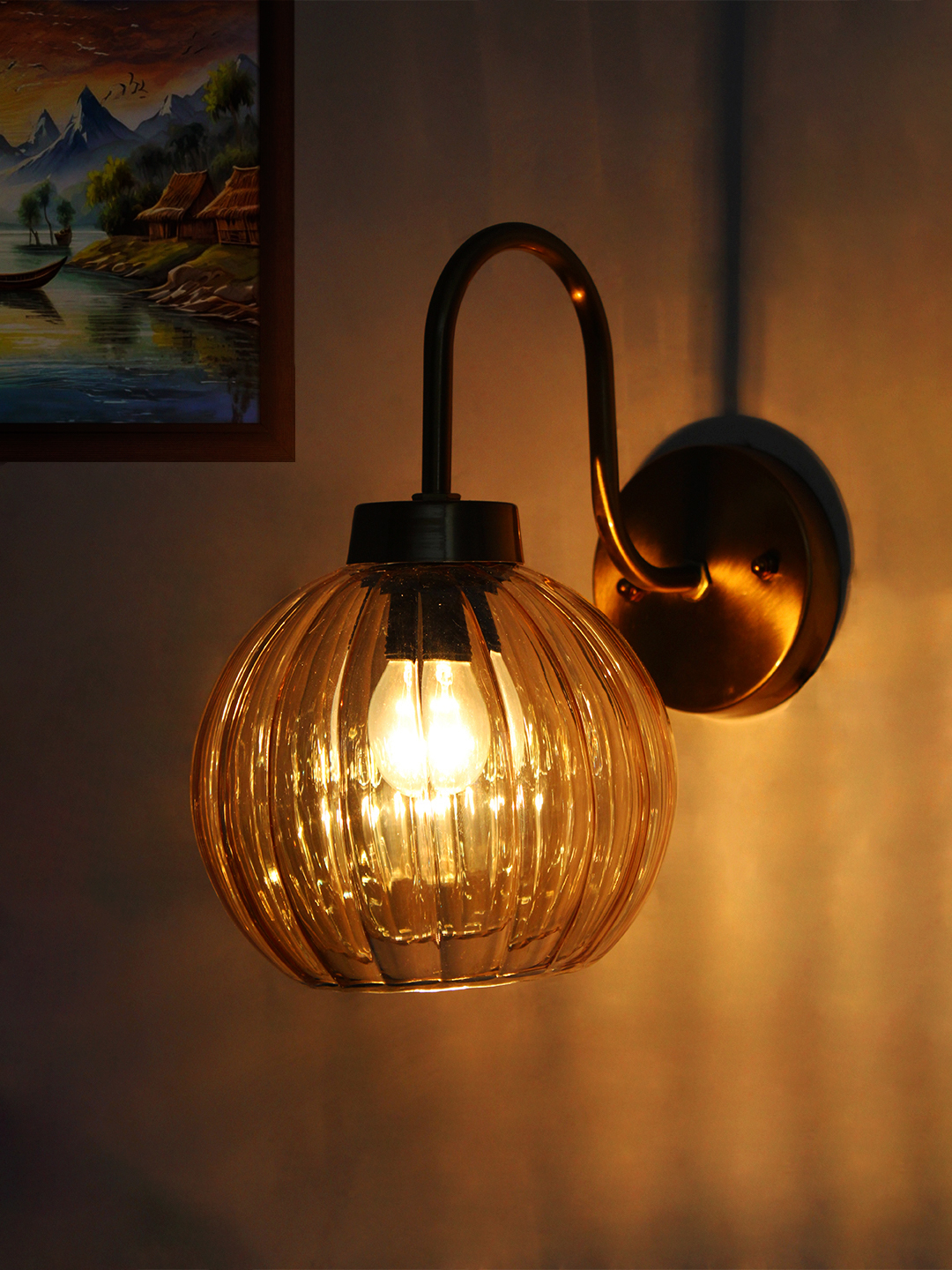 Decorative Brass Wall Sconce Ribbed Amber Glass Brass wall sconce with curved arm and ribbed amber glass globe shade mounted on a white wall, providing warm ambient lighting.