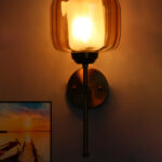 Modern light fixture wall sconce with amber glass shade and brass finish, casting warm light beside a sunset landscape wall art on a white wall
