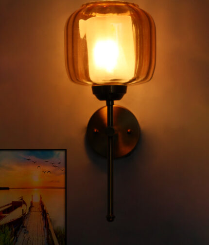 Modern light fixture wall sconce with amber glass shade and brass finish, casting warm light beside a sunset landscape wall art on a white wall