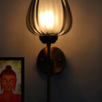 Wall-mounted lamp with a smoked glass shade and brushed gold metal base, providing soft ambient lighting on a white wall.