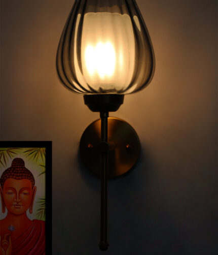 Wall-mounted lamp with a smoked glass shade and brushed gold metal base, providing soft ambient lighting on a white wall.