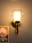 Gold wall sconce with curved arm and textured glass shade mounted on a white wall, providing warm ambient lighting.