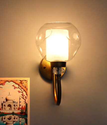 Gold wall sconce with curved arm and textured glass shade mounted on a white wall, providing warm ambient lighting.