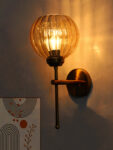 Elegant brass wall light with ribbed amber glass shade, modern wall sconce mounted on a white wall providing warm ambient lighting for stylish interiors