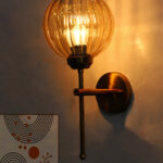 Elegant brass wall light with ribbed amber glass shade, modern wall sconce mounted on a white wall providing warm ambient lighting for stylish interiors